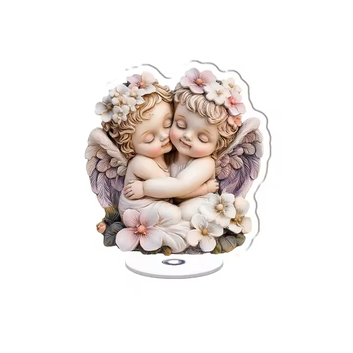Una figura acrílica giratoria que presenta dos ángeles bebés con alas plegadas abrazándose, rodeados de flores vibrantes sobre un fondo blanco. - 1