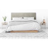 Ambiente de dormitorio con cabecero de cama tapizado en gris, una cama, mesitas, alfombra, etc